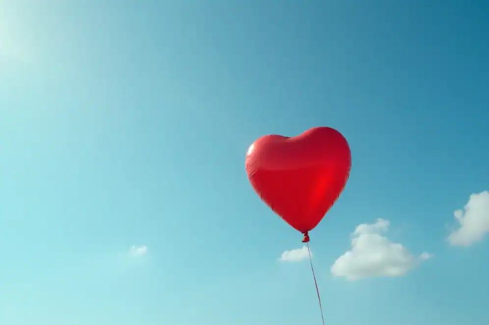 A heart-shaped balloon floats in the sky.
